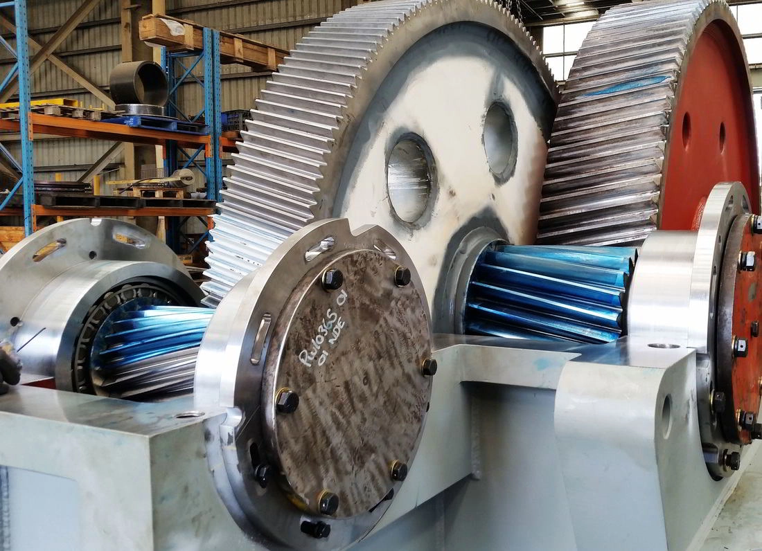 A large industrial gearbox assembly with helical gear sets and machined pinion shafts in the workshop
