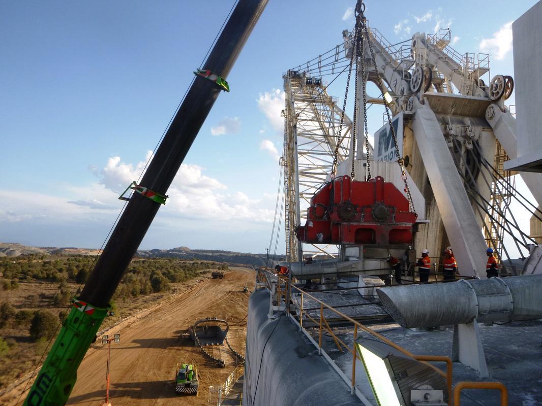 Crane lowering a red propel gear case onto the Marion 8750 dragline during an on-site change-out, crews in hi-vis on the platform