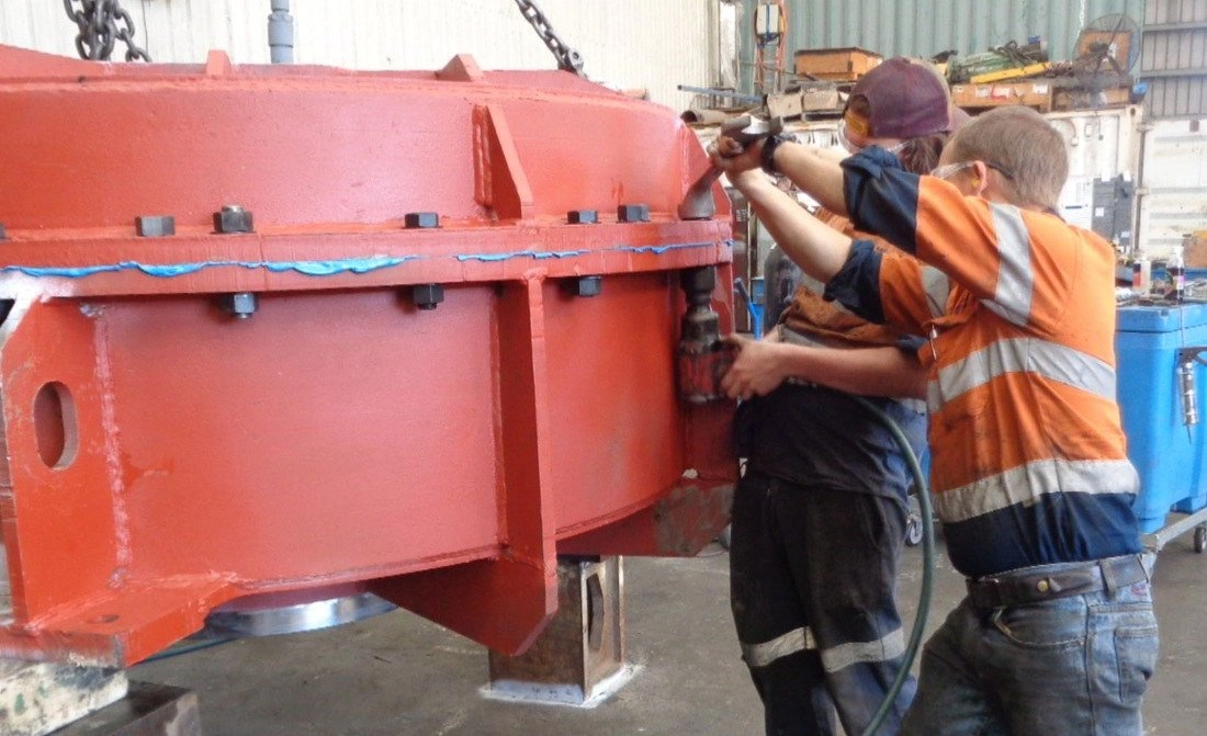 Two ABC Heavy Engineering fitters in hi-vis working together on a large red-painted machinery casing in the workshop