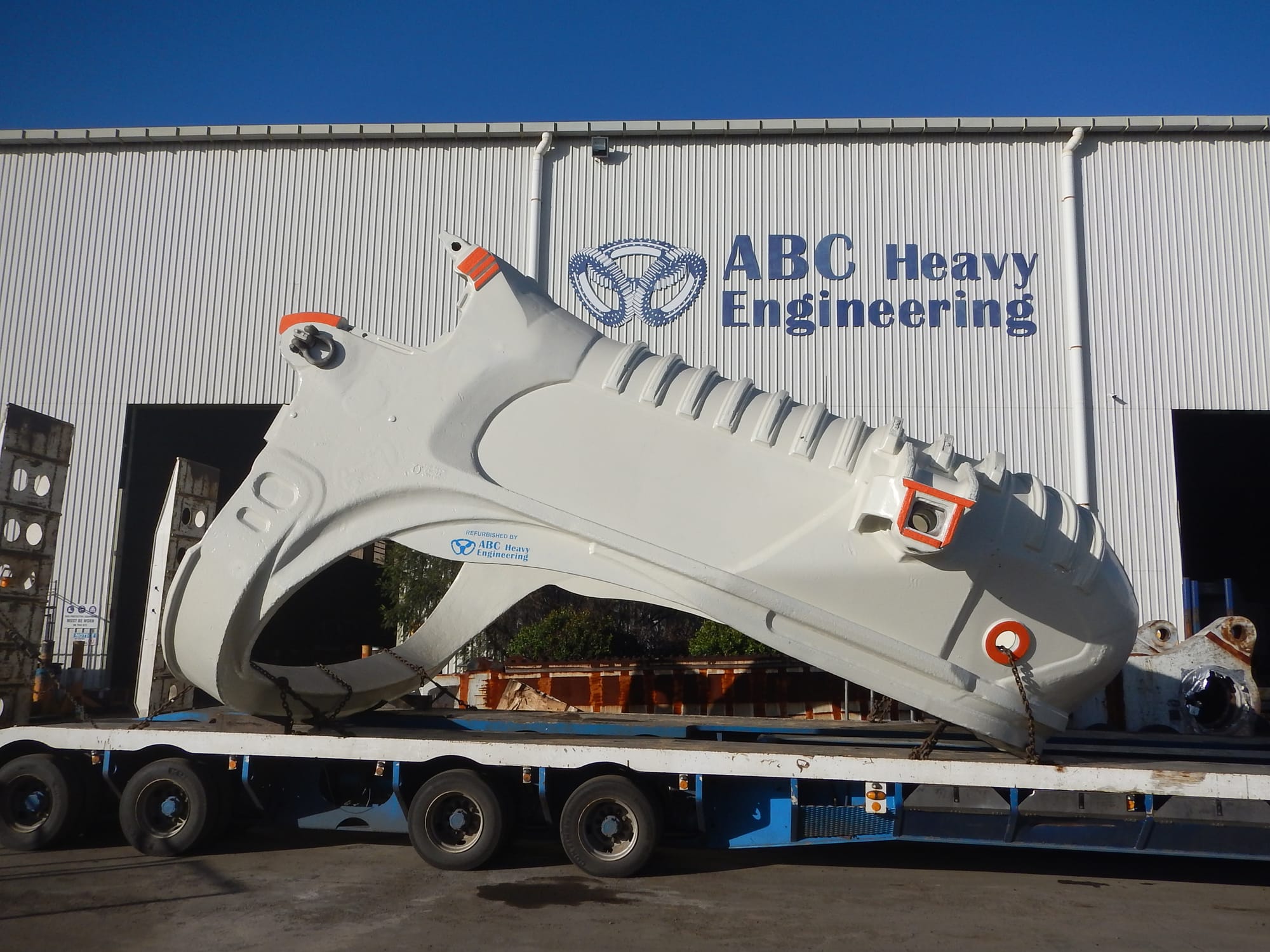 Refurbished white dragline bucket with a Refurbished by ABC Heavy Engineering decal, loaded on a low loader outside the signed Paget workshop