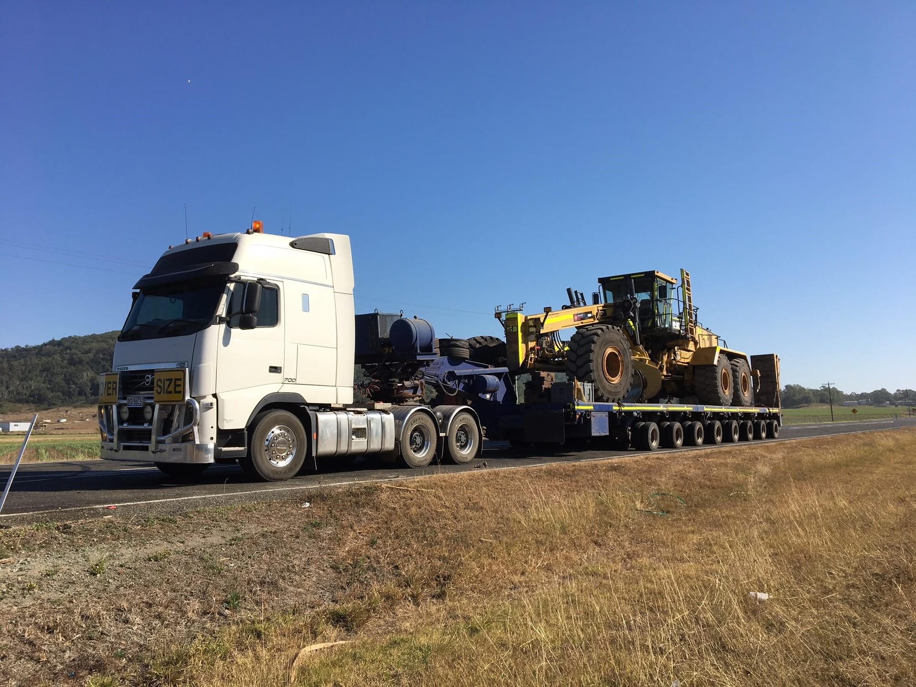 Caterpillar grader on a low loader behind a Volvo FH700 prime mover on a Queensland highway